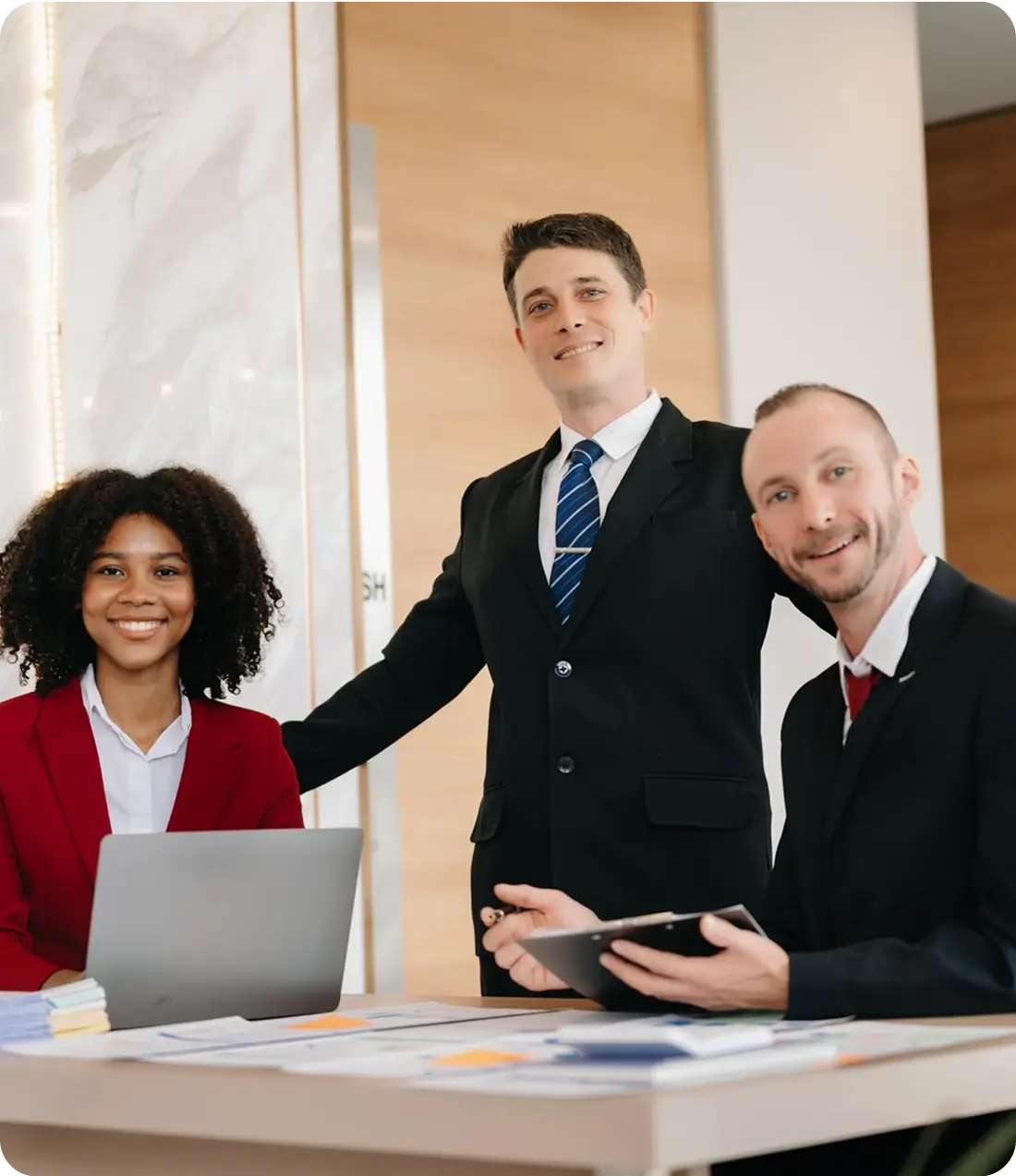 Three insruance professionals in business attire collaborating at a desk with a laptop and documents.