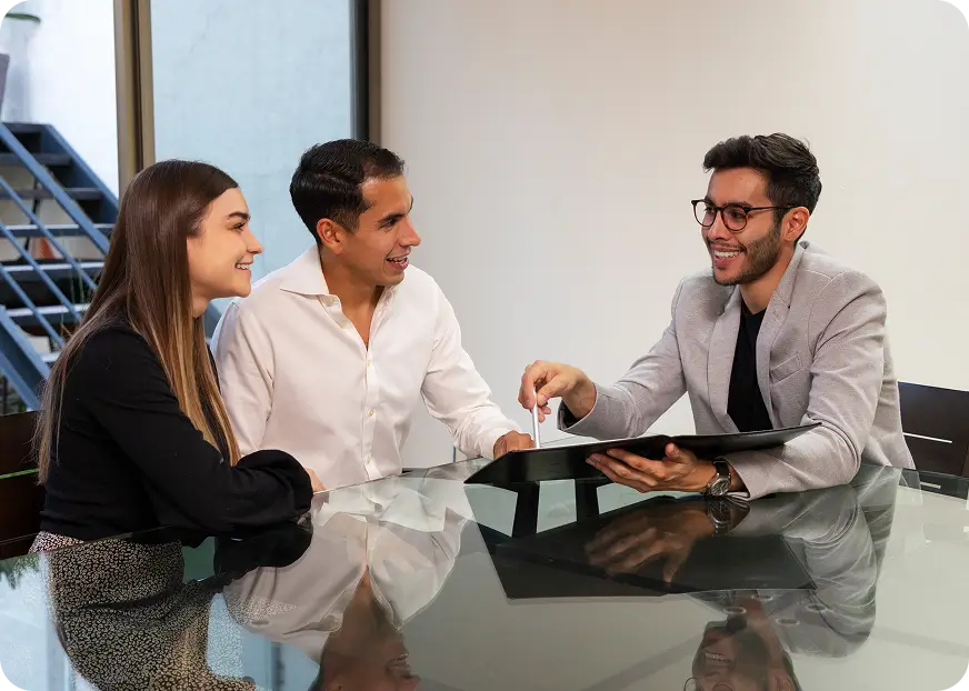 Insurance advisor meeting with a couple at a desk, reviewing policy details together on a tablet in a professional office setting